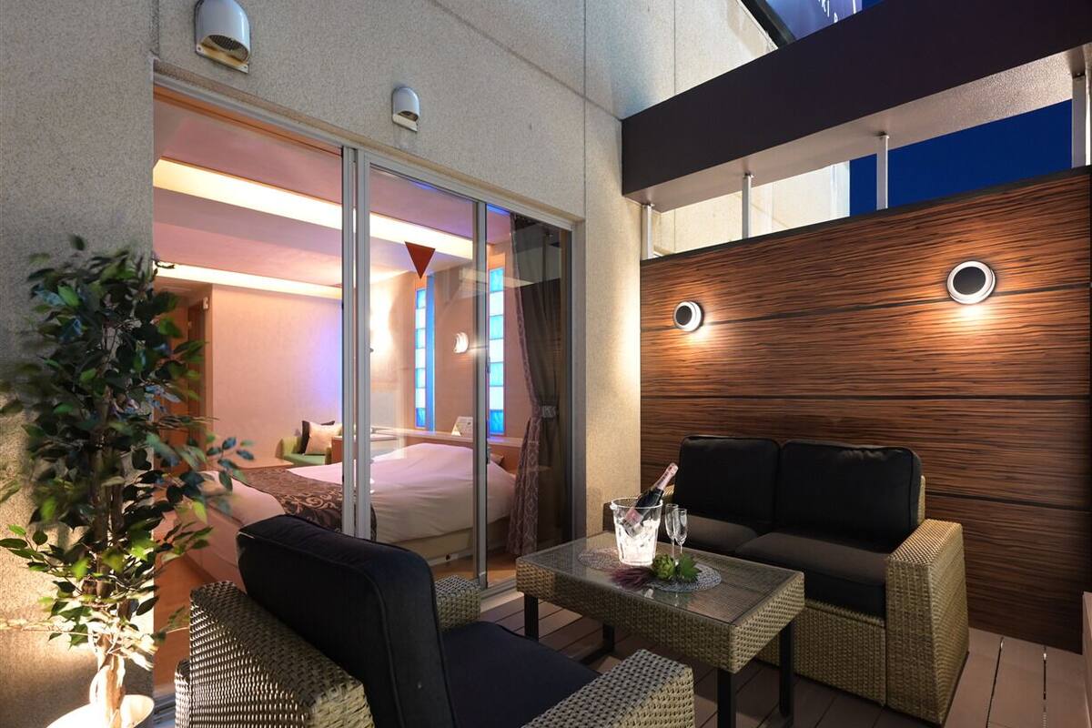 A modern outdoor seating area with wicker furniture, a glass table, and a wooden accent wall.