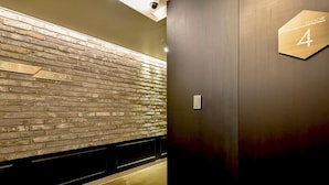 A hallway with a brick wall and a wooden floor. There is a sign indicating 'Floor 4' and a door with a number plate. - Ulsan Hotel 109 (Ulsan)