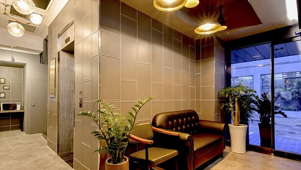 A modern lobby with a leather sofa, potted plants, and a large window offering a view of the street. - Ulsan Hotel 109 (Ulsan)