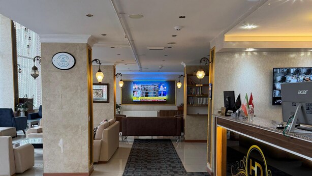 Un vestíbulo de hotel con mostrador de recepción, una pantalla grande que muestra información, zonas de estar y piso alfombrado.