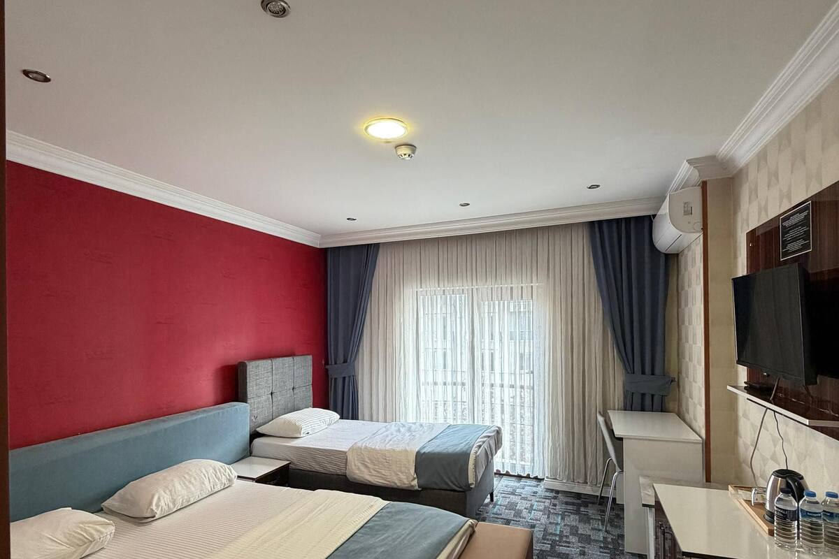 Hotellihuone, jossa on kaksi sänkyä, työpöytä, televisio ja ikkuna, jossa on verhot.