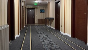 Un pasillo de hotel con pisos alfombrados, puertas de madera y un candelabro en el techo.