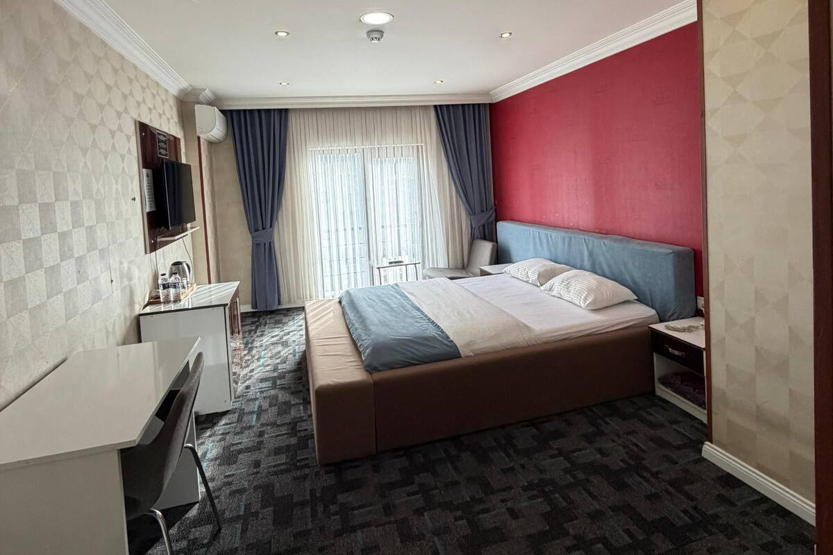 Hotellihuone, jossa on sänky, työpöytä, tuoli, televisio ja ikkuna, jossa on verhot.