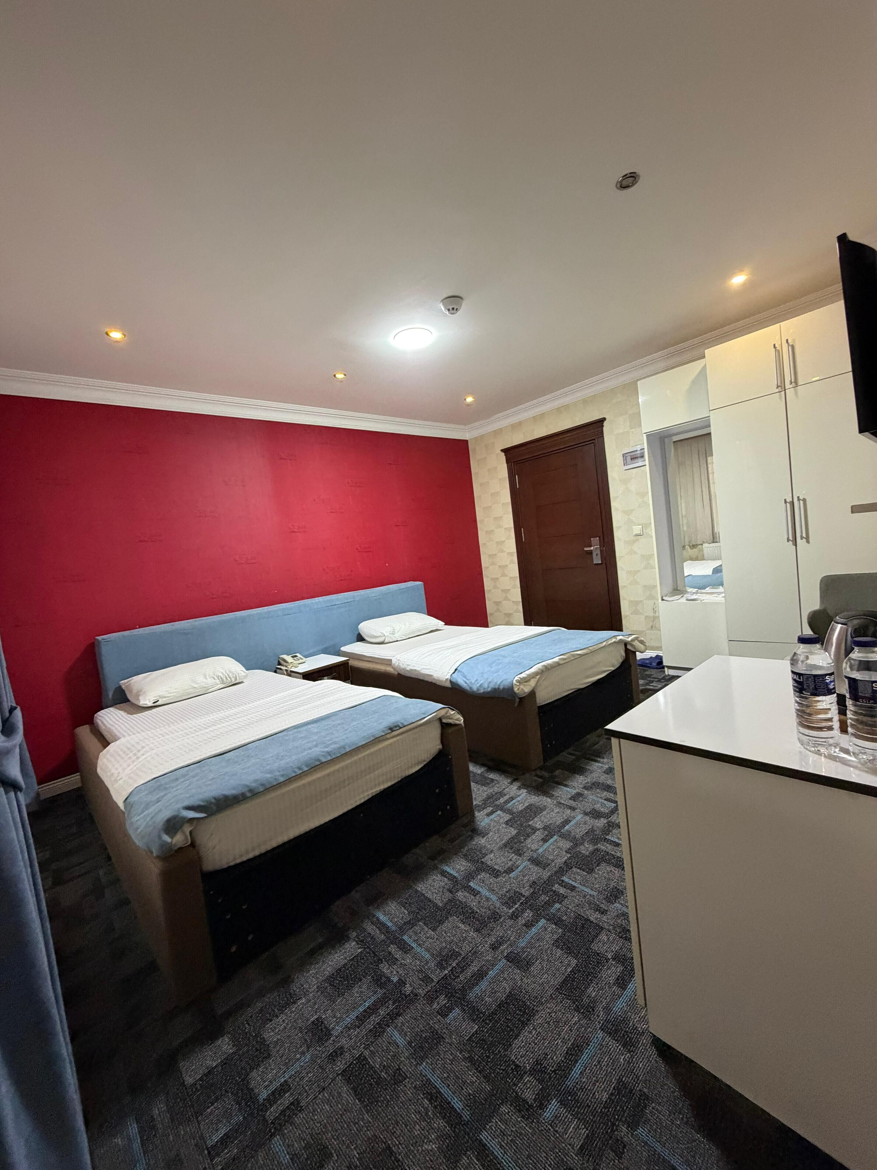 A hotel room with two single beds, a desk, a wardrobe, and a television.