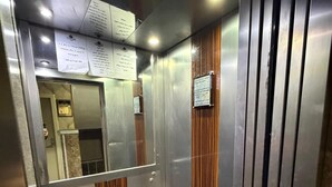 Interior de ascensor con paredes metálicas, paneles de madera, suelo reflectante y una barandilla.