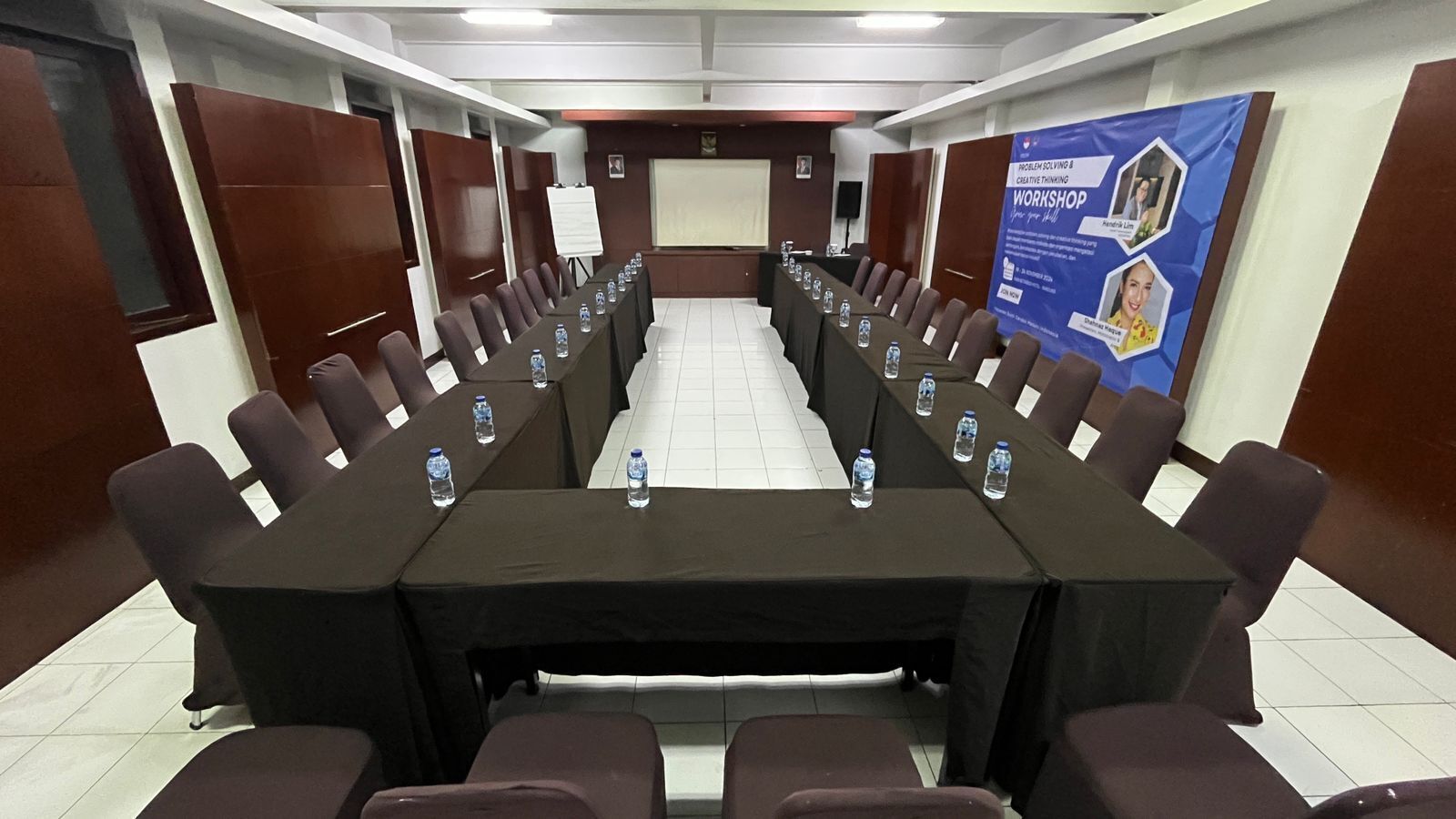 Un salón de conferencias con una larga mesa, sillas y botellas de agua.