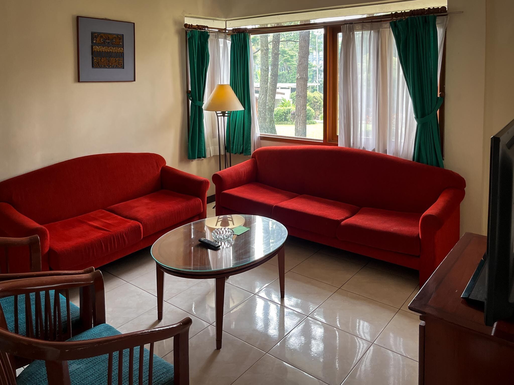 A living room with two red sofas, a glass coffee table, a wooden chair, a floor lamp, and a TV.