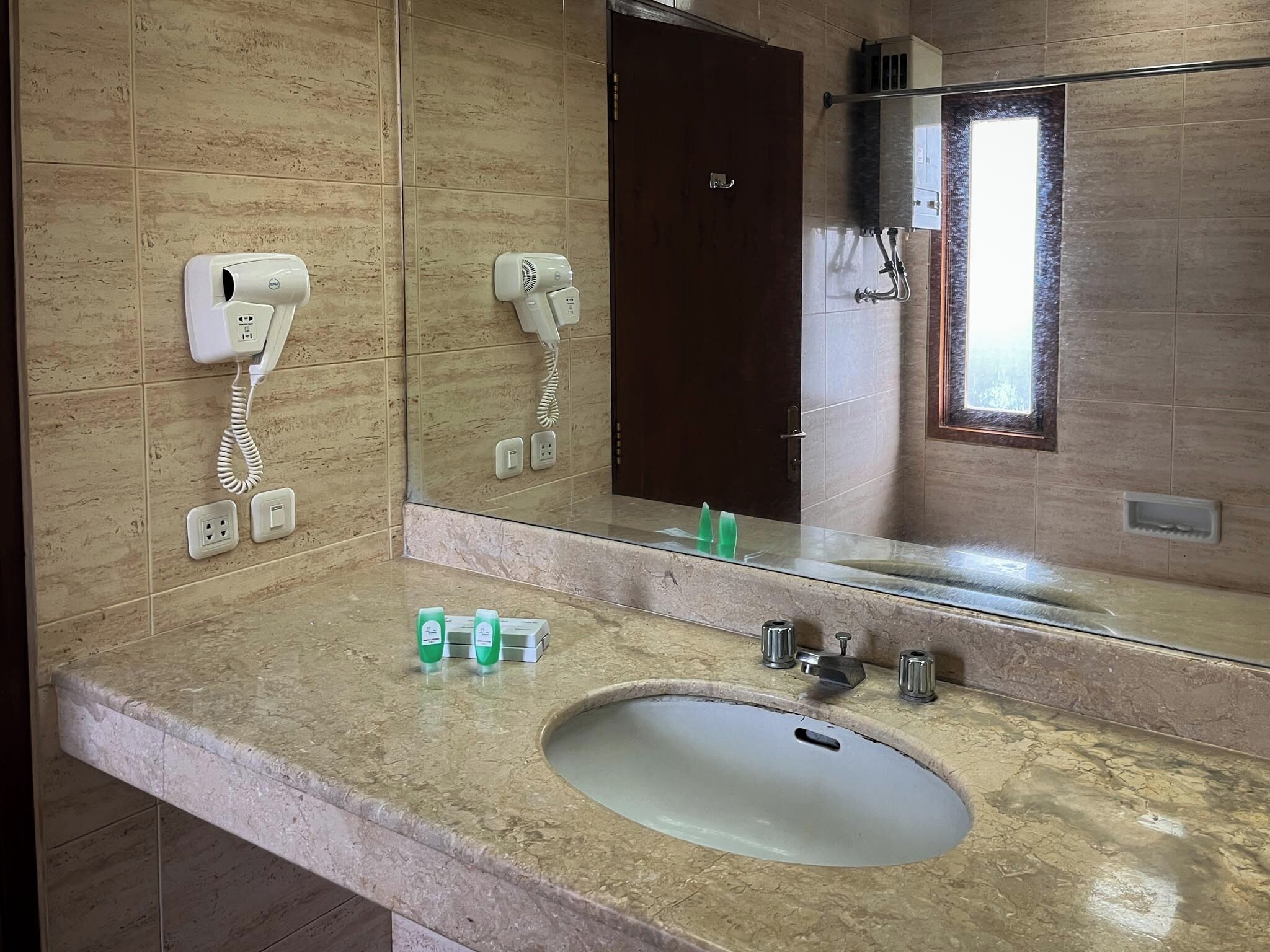 Une salle de bain équipée d’un lavabo, d’un miroir et de deux sèche-cheveux fixés au mur.