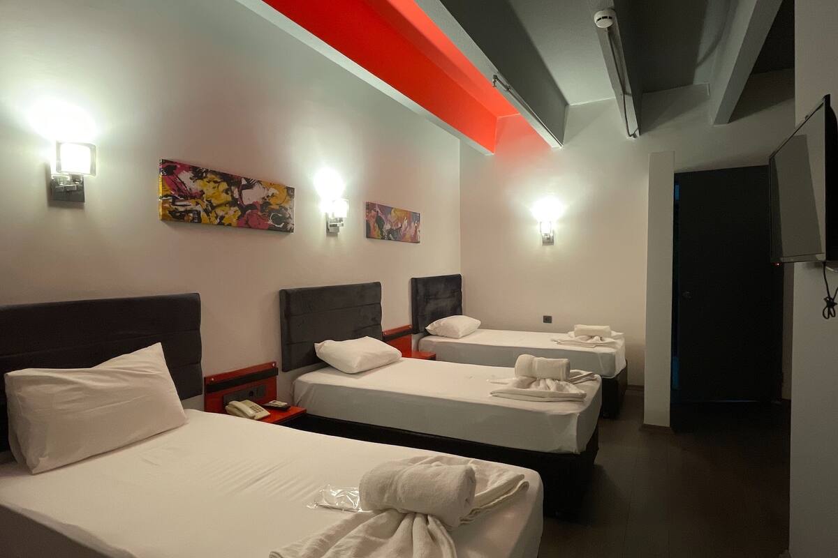 A hotel room with two beds, a TV, artwork on the wall, and a red accent wall.