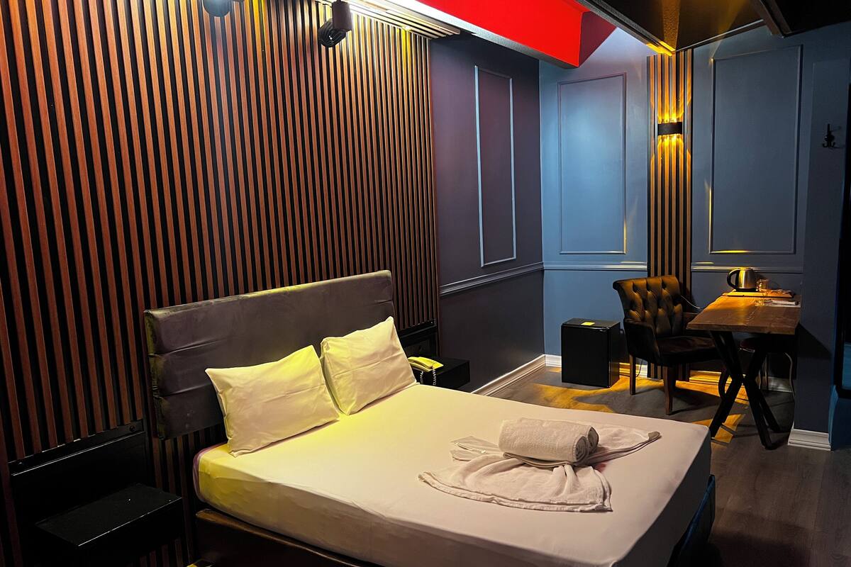 A hotel room with a bed, bedside table, and a small desk with a chair.