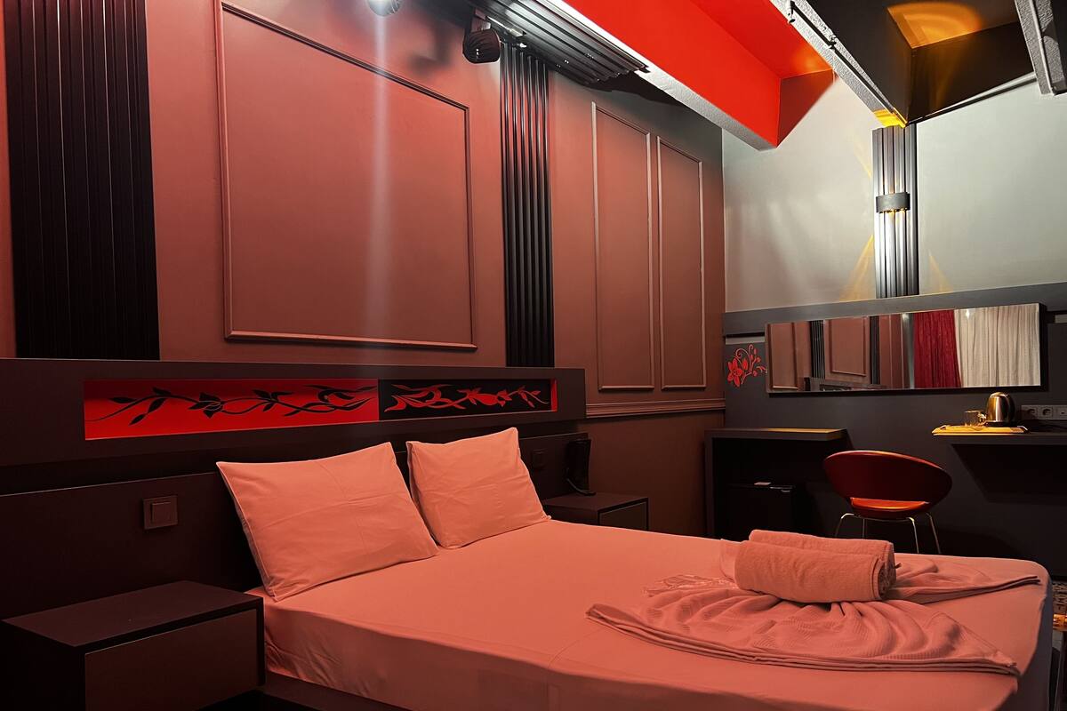 A hotel room with a bed, nightstands, a desk, and a chair.