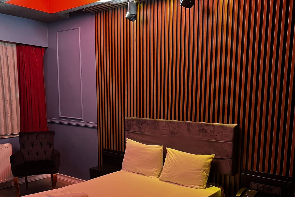 A hotel room with a bed, a chair, a nightstand with a phone, and a window with curtains.