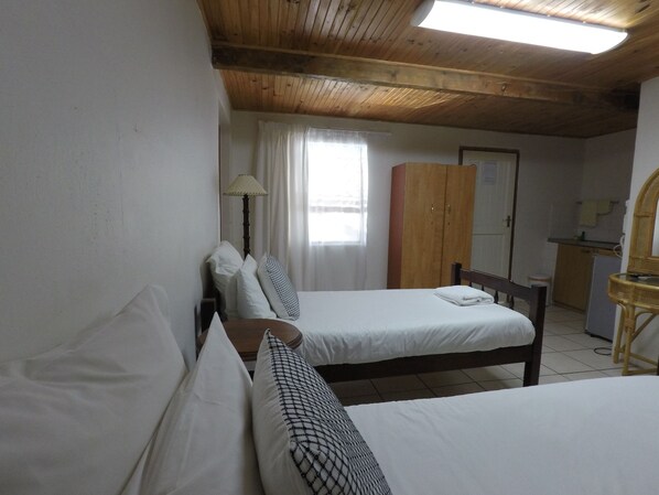 A bedroom with two beds, a wardrobe, a desk, and a mirror.