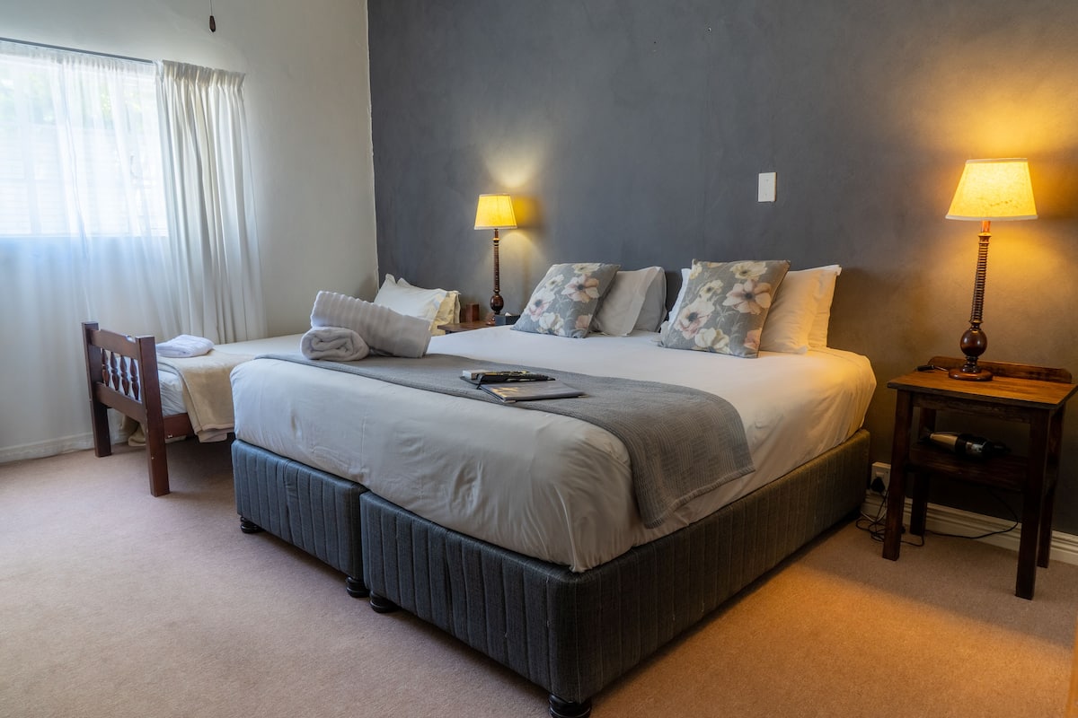 Una cama bien hecha con almohadas, una mesita de noche con lámpara y una silla.