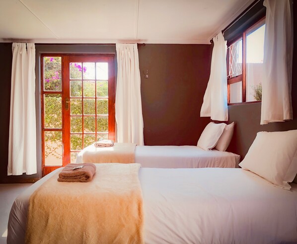A hotel room with two beds, a window with curtains, and a view of greenery outside. - Selborne Bed and Breakfast (East London)