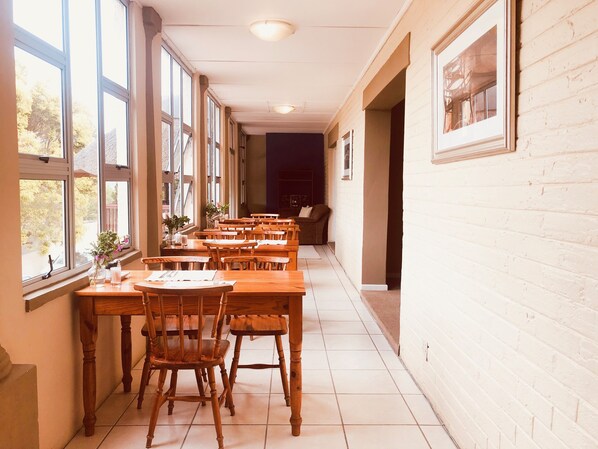 A long dining area with wooden tables and chairs, large windows, and a brick wall. - Selborne Bed and Breakfast (East London)