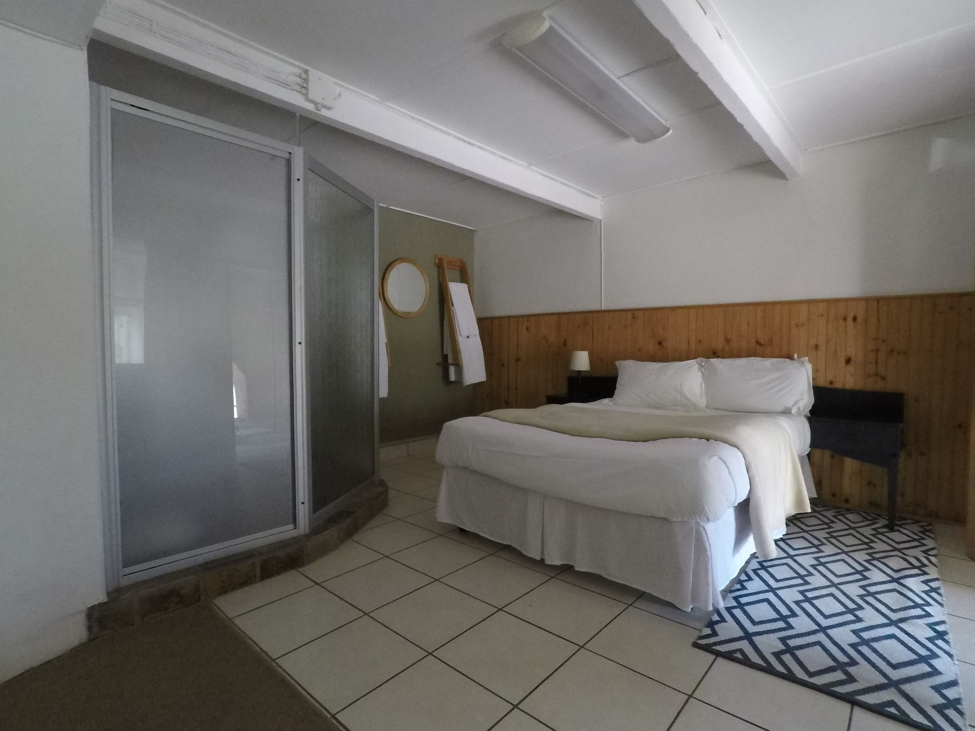 Una habitación de hotel con cama, cabecera de madera, mesita de noche, espejo y puerta corredera.