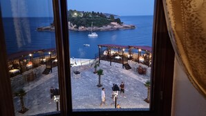 A view from a window overlooking a coastal area with a dining terrace, a small island, and a body of water. - Hotel Kulla e Balshajve (Ulcinj)