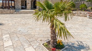 Un bâtiment en pierre avec une enseigne indiquant la présence d’un restaurant, un palmier et un banc au premier plan.