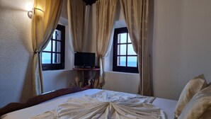 Une chambre avec un lit, deux fenêtres avec des rideaux, un téléviseur posé sur un meuble et une vue sur la mer.