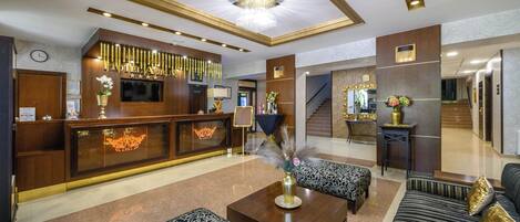 Un vestíbulo de hotel con una recepción, una zona de estar y una escalera.