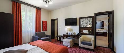 Habitación de hotel con una cama, dos sillones, un escritorio con lámpara, televisión y un baño visible a través de una puerta abierta.