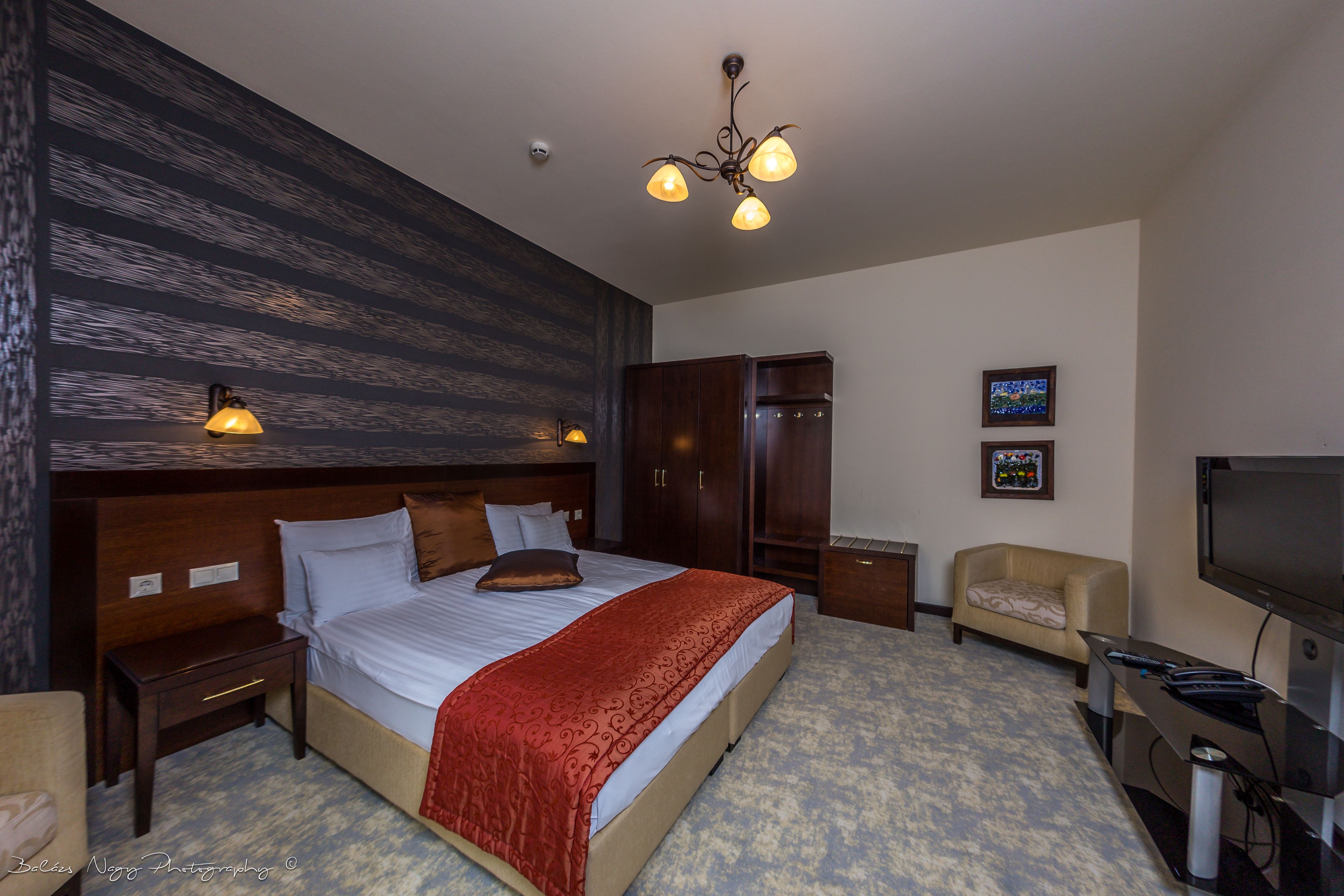 Habitación de hotel con una cama grande, cabecero de madera, televisor, sofá y candelabro.