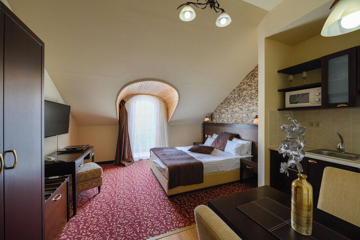 A hotel room with a bed, a desk, a TV, a microwave, and a sink.