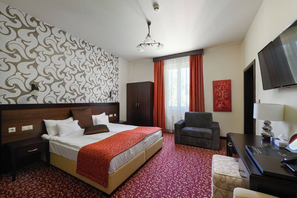 A hotel room with a large bed, a desk, a chair, and a TV.