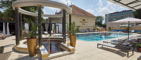 Zona de piscina hotelera con sillones reclinables, una bañera de hidromasaje y una zona de estar cubierta.
