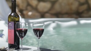 Une bouteille de vin et deux verres de vin rouge sont posés sur une table, près d’un bain à remous.
