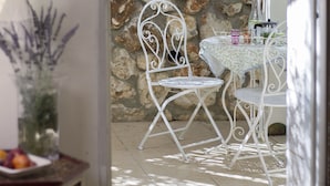 Un mur de pierre, une chaise en métal, une table recouverte d’une nappe à motifs et un vase rempli de fleurs.