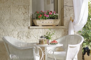 A wicker table with chairs, a potted plant, a watermelon slice, and a small window with flowers.
