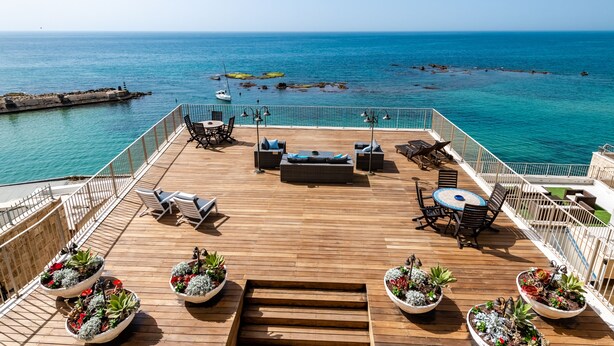 A wooden deck with outdoor seating, potted plants, and a view of the sea.