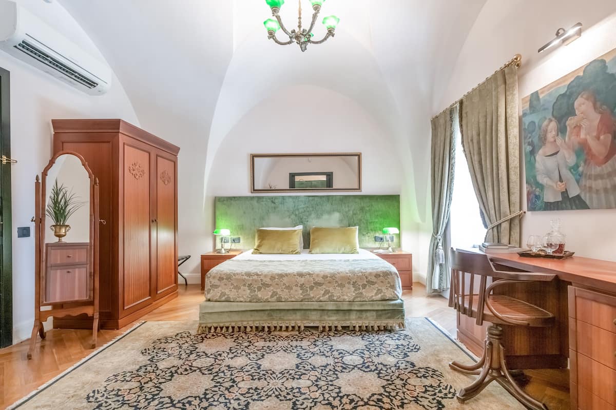 Une chambre à coucher avec un grand lit, un bureau, une chaise, une armoire, un lustre et un tableau au mur.