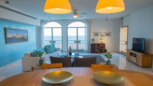 A modern living room with a dining table, sofas, and large windows offering a view.