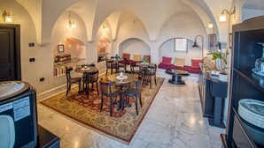 A spacious interior with arched ceilings, a dining area with round tables and chairs, a seating area with red cushions, and a television on the right.