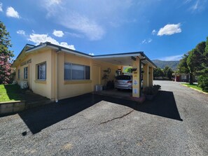 Ein Motel mit überdachtem Parkplatz, einem eingeschossigen Gebäude und einem Berg im Hintergrund.