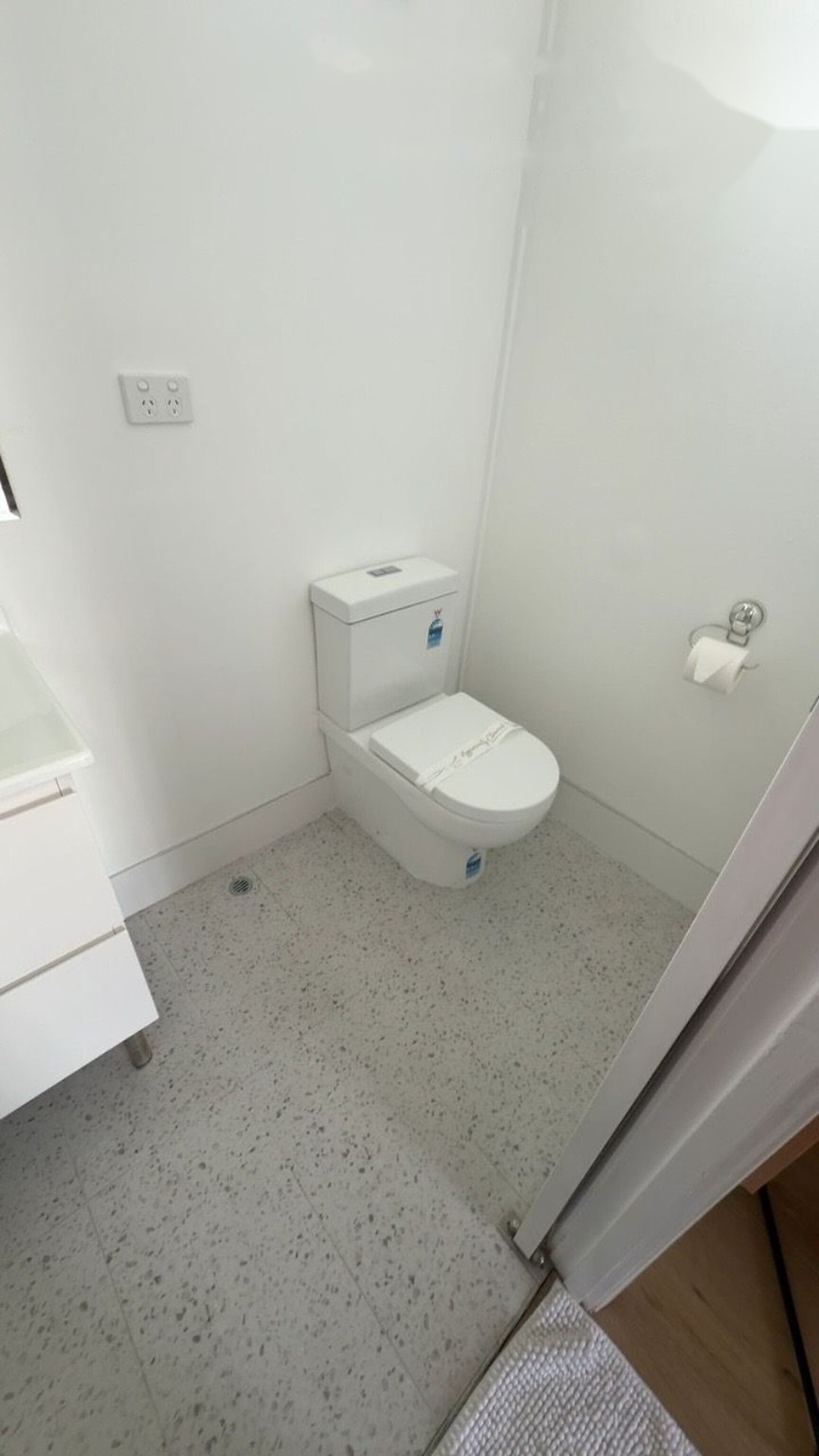 Une petite salle de bain blanche, équipée de toilettes, d’un lavabo et d’un espace douche.