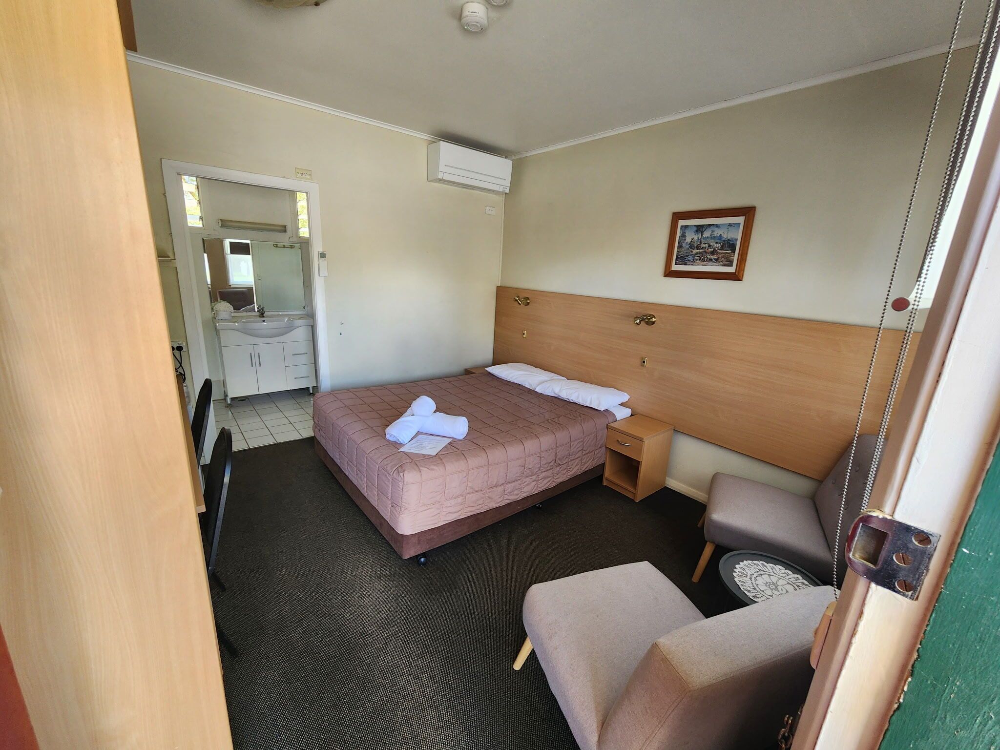 A hotel room with a bed, bedside table, chair, and a bathroom visible through an open door.