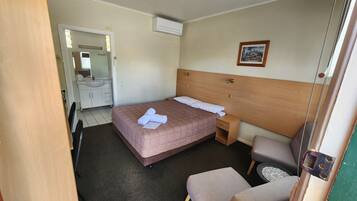 A hotel room with a bed, bedside table, chair, and a bathroom visible through an open door.