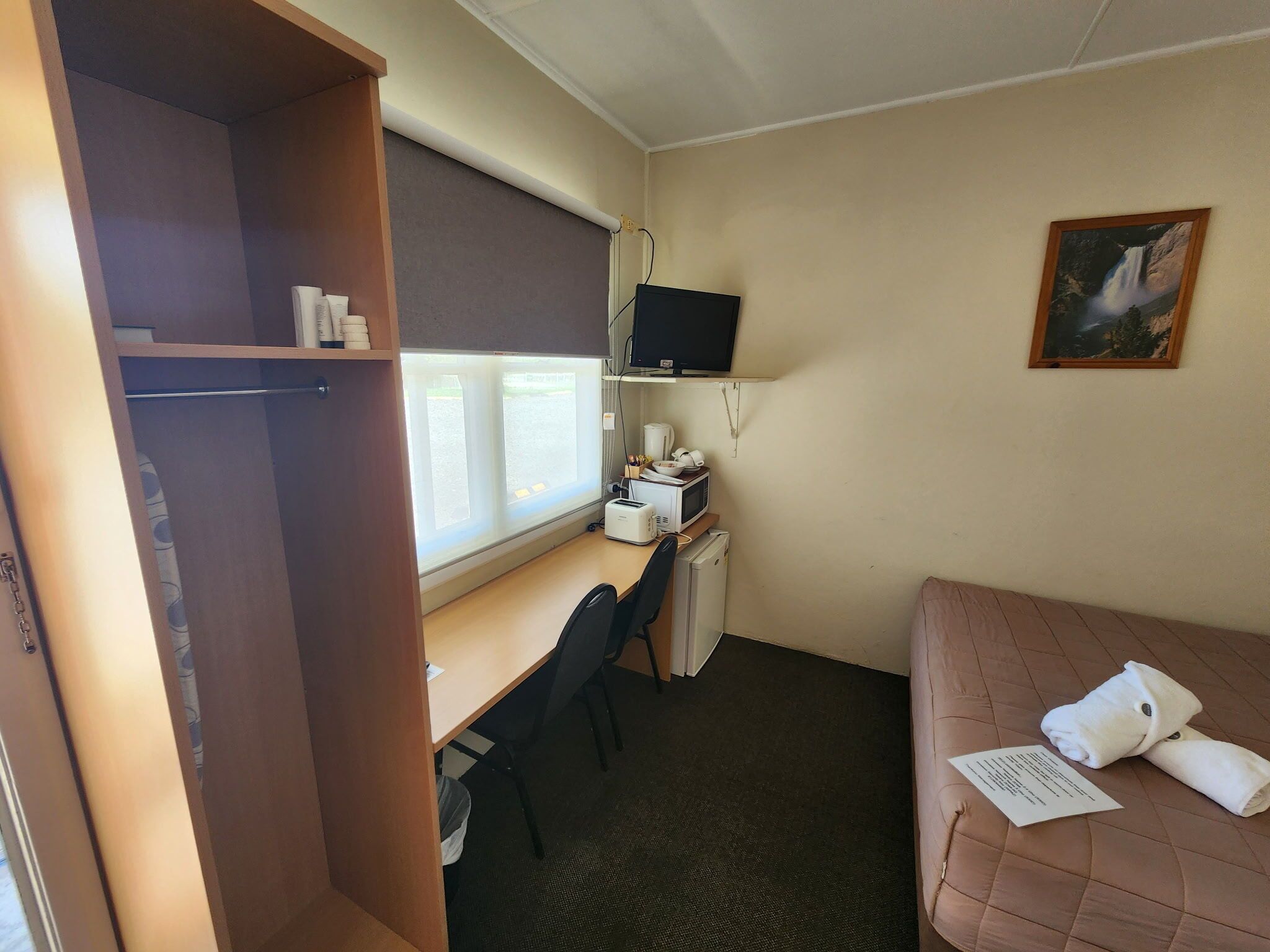 Habitación pequeña con cama, escritorio, televisión y ventana.