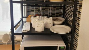 Une cuisine équipée d’un micro-ondes, d’un grille-pain et d’une bouilloire, placés sur une étagère, ainsi que d’un saladier et d’assiettes sur le plan de travail.