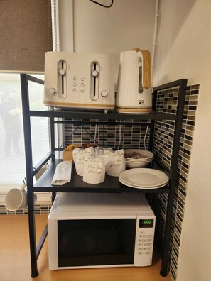 Une cuisine équipée d’un micro-ondes, d’un grille-pain et d’une bouilloire, placés sur une étagère, ainsi que d’un saladier et d’assiettes sur le plan de travail.