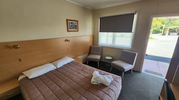 Hotellihuoneessa on sänky, kaksi nojatuolia, pieni pöytä, ikkuna, jossa on verho, ja taulu seinällä.