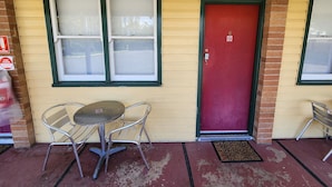 Un bâtiment avec une porte rouge, deux fenêtres à vitres dépolies et une petite table avec deux chaises à l’extérieur.