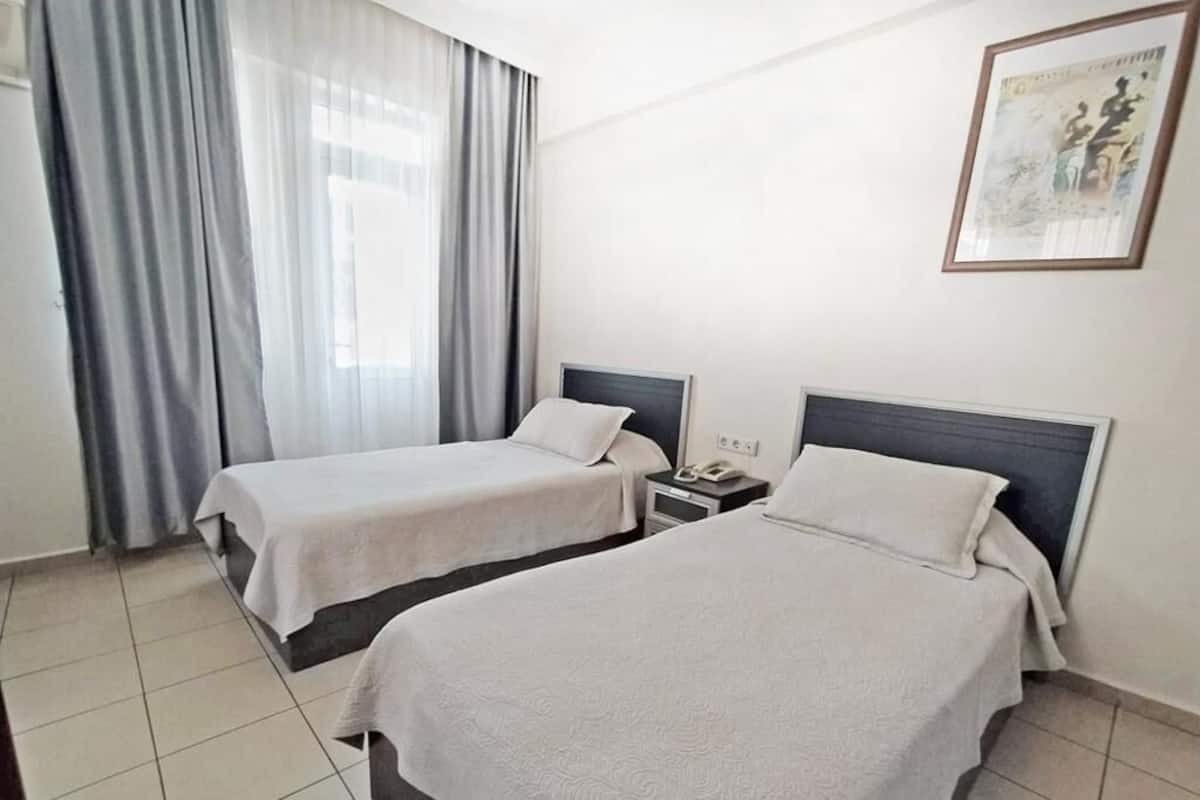 A hotel room with two beds, a bedside table with a phone, and a window with curtains.