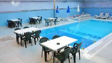 Et poolområde med liggestole og borde, et overdækket siddeområde samt en pool, hvor der står 'DIAMON' i vandet.