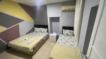 A small, well-lit room with two beds, a bedside table, a wall-mounted air conditioner, and a geometric-patterned wall.