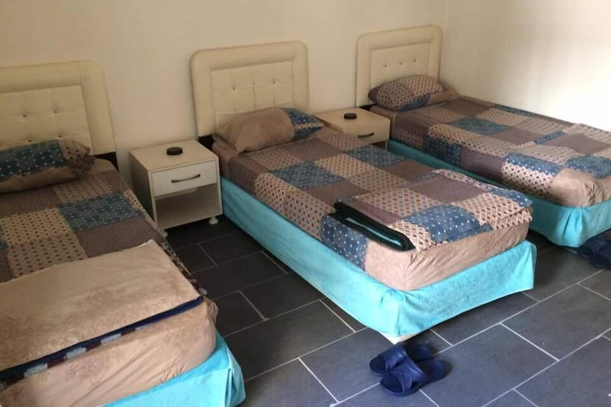 A room with three single beds, each with a headboard, a nightstand, and a pillow.